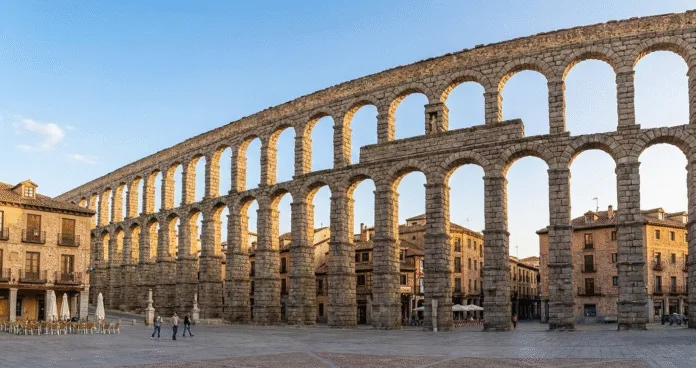 Roman aqueduct in Segovia with old town buildings, popular day trip from Madrid Spain
